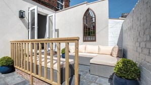 Eine Terrasse mit Holzzaun, einer gepolsterten Sitzecke und einem kleinen Fenster mit dekorativem Rahmen.