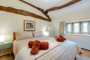 Ein Schlafzimmer mit einem Bett, karierter Bettwäsche, einem Bild an der Wand, einem Fenster mit Vorhängen und einem Nachttisch mit Lampe.