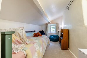 Une chambre à coucher avec un lit, une commode verte, une fenêtre avec des rideaux et un fauteuil en forme de sac de haricots bleu.