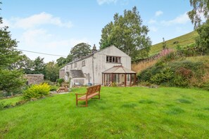 Une maison avec un grand jardin, une véranda et un banc.