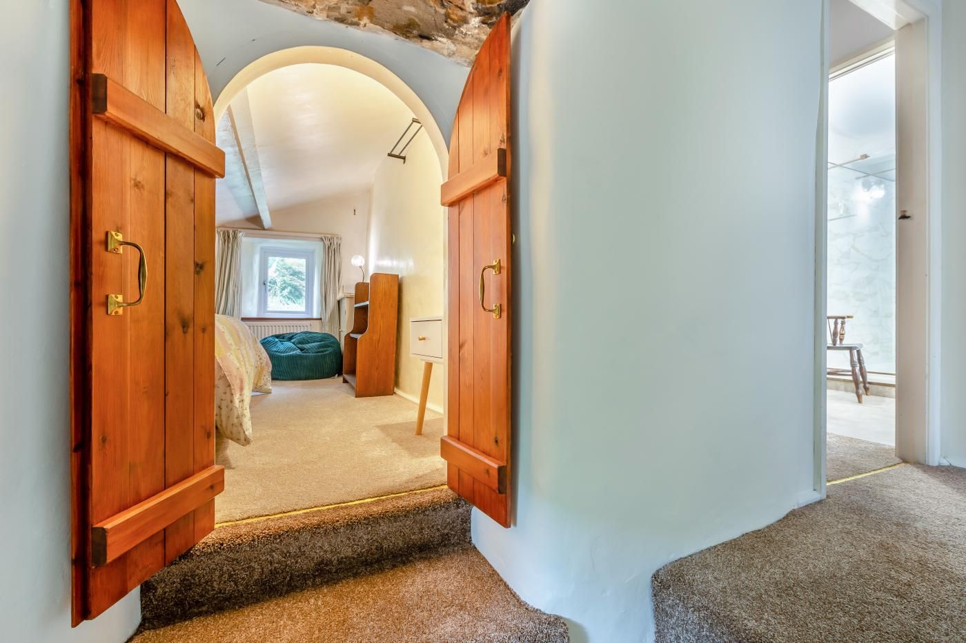 A hallway leading to a bedroom with a window, a green bean bag, and a wooden wardrobe.