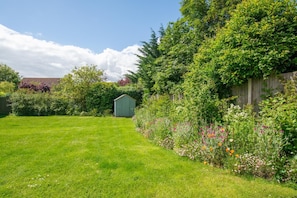 A well-maintained garden with a small shed, a wooden fence, and a variety of flowering plants.