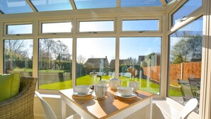Un invernadero con una mesa dispuesta para el té, muebles de mimbre y vistas a un jardín trasero.