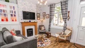 Ein Wohnzimmer mit Kamin, einer Couch, einem Sessel, einem Fernseher und einem gemusterten Teppich.