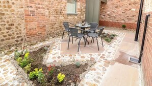 Eine Terrasse mit Backsteinmauer, Steinboden und Tisch mit Stühlen.