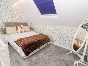 A bedroom with a skylight, a bed with a leopard print blanket, a white dresser, and a mirror.