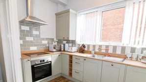 Eine moderne Küche mit weißen Schränken, einer Holz Arbeitsplatte, einem eingebauten Backofen und einem Fenster mit Jalousien.