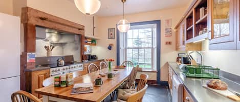 Una cocina con armarios de madera, una mesa de comedor, sillas, una estufa y lámparas colgantes.