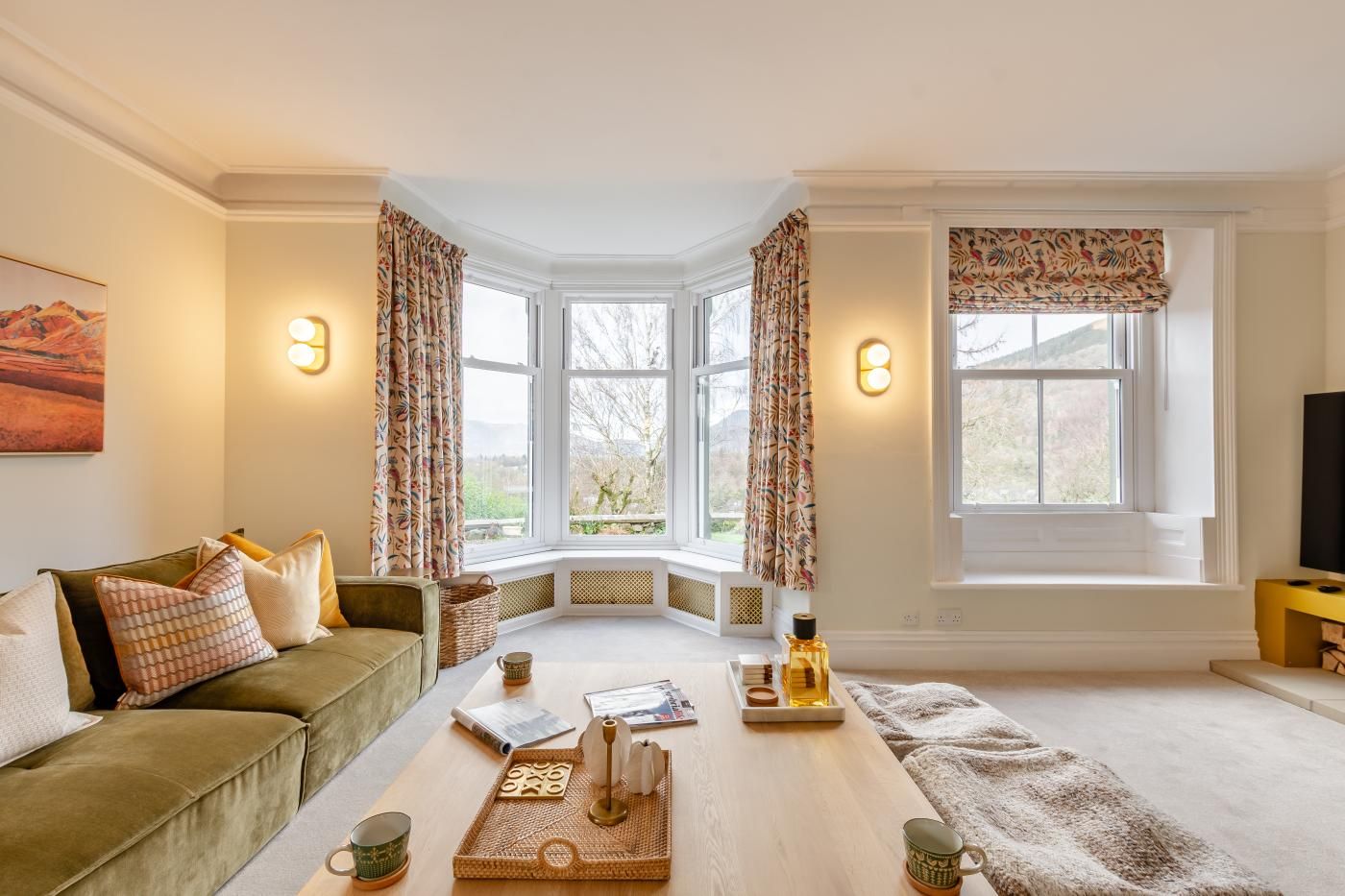 A cozy living room with a green sofa, a wooden coffee table, and a bay window with curtains.