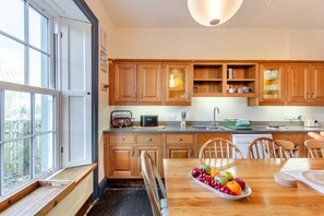 A modern kitchen with wooden cabinets, a built-in oven, and a dining area with a fruit bowl. - 5 Bed in Keswick (oc-h33619) (Keswick)