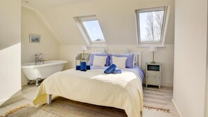 Quarto com uma cama grande, uma banheira, duas mesas de cabeceira e um claraboia.