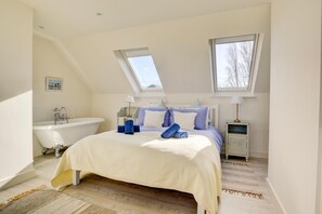 Ein Schlafzimmer mit einem großen Bett, einer Badewanne, zwei Nachttischen und einem Oberlicht.
