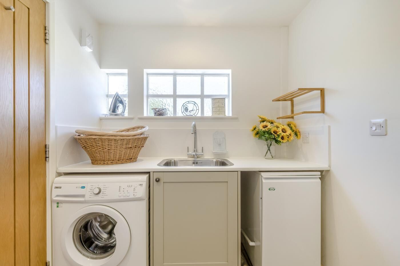 A compact laundry room with a washing machine, a dryer, a sink, and a window with a view.