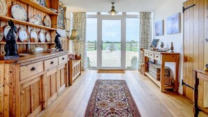 Una habitación amplia con suelo de madera, un ventanal con vistas a un paisaje rural y una chimenea tradicional.