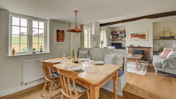 A dining area with a wooden table and chairs, a hanging pendant light, and a view of a garden through large windows. - 2 Bed in Little Barningham (oc-1817) (Little Barningham)
