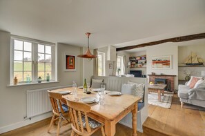 A dining area with a wooden table and chairs, a hanging pendant light, and a view of a garden through large windows. - 2 Bed in Little Barningham (oc-1817) (Little Barningham)