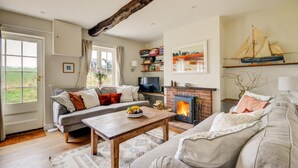 A cozy living room with a fireplace, a sofa, a coffee table with fruit, and a bookshelf. - 2 Bed in Little Barningham (oc-1817) (Little Barningham)