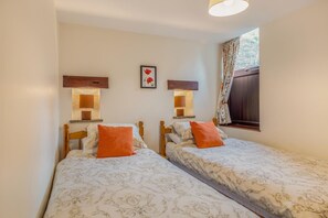 Ein Doppelzimmer mit zwei Betten, jeweils mit einem hölzernen Kopfteil, einem Nachttisch, einer Lampe und einer zudeckenden Bettdecke mit Blumenmuster.