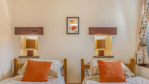 A room with two beds, each with a wooden headboard and an orange pillow. There are wall-mounted lamps above each bed, and a framed picture hangs between them. - 2 Bed in Earl Sterndale (oc-p33566) (Earl Sterndale)