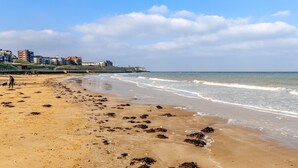 Una playa arenosa con olas, un muelle y edificios al fondo.