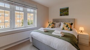 Habitación de hotel con un ventanal grande, una cama con una manta verde y un cuadro en la pared.