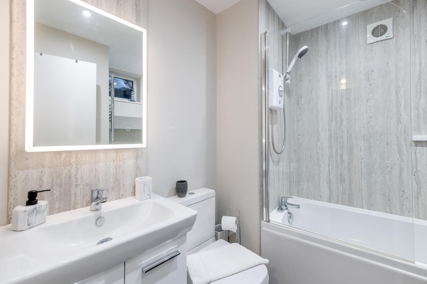 Un baño moderno con un espejo grande, dos lavamanos, inodoro y cabina de ducha con paredes de vidrio.