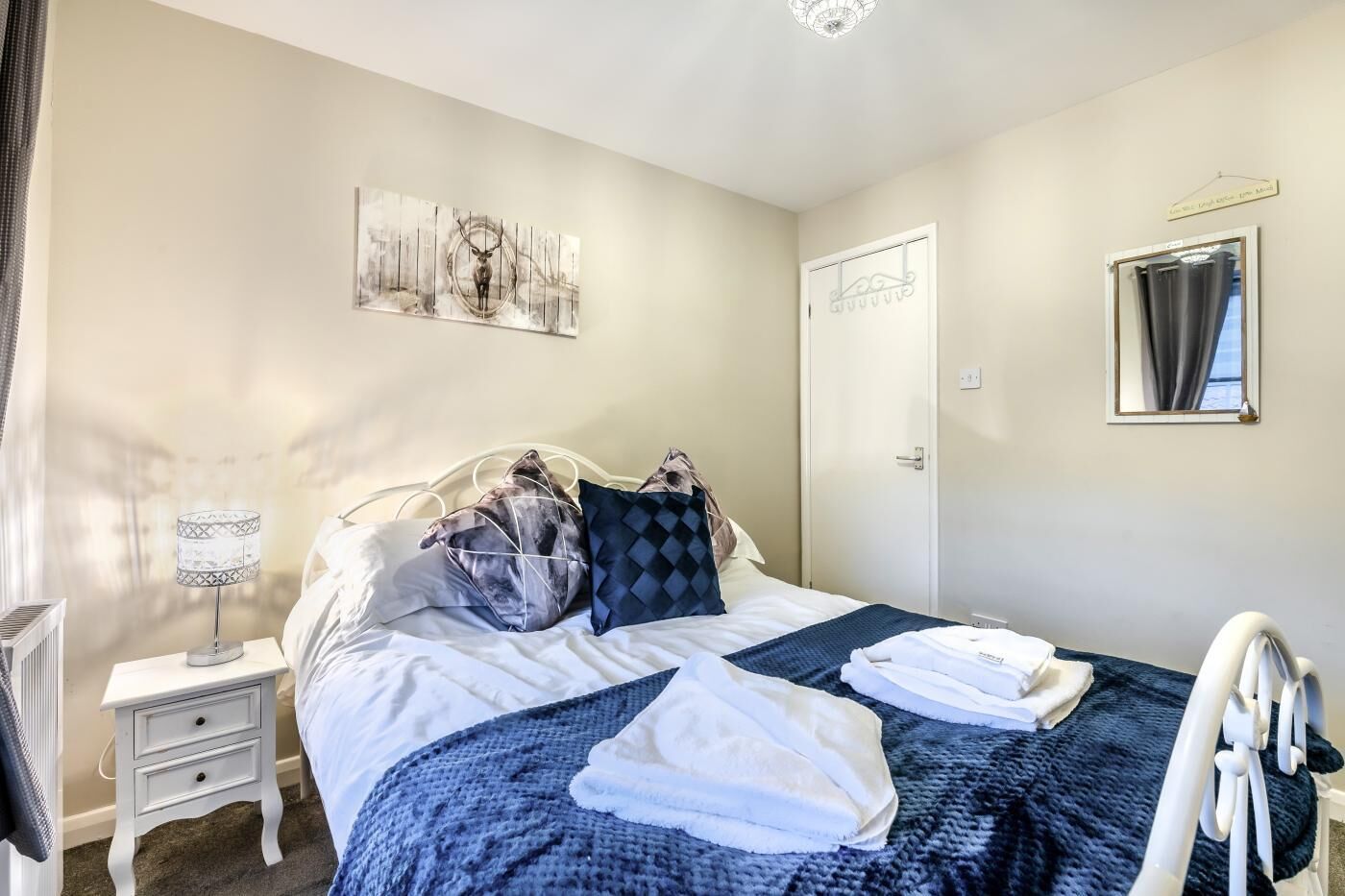 Une chambre d’hôtel avec un lit, une table de chevet avec une lampe, une porte et une œuvre d’art accrochée au mur.