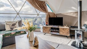 Une pièce accueillante aménagée comme une tente, avec un canapé, un téléviseur à écran plat, un poêle à bois et une vue sur le paysage.