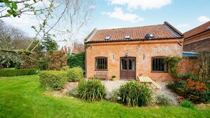 A brick house with a tiled roof, a front door, and a small garden with a bench and potted plants. - 2 Bed in Erpingham (oc-2278) (Erpingham)