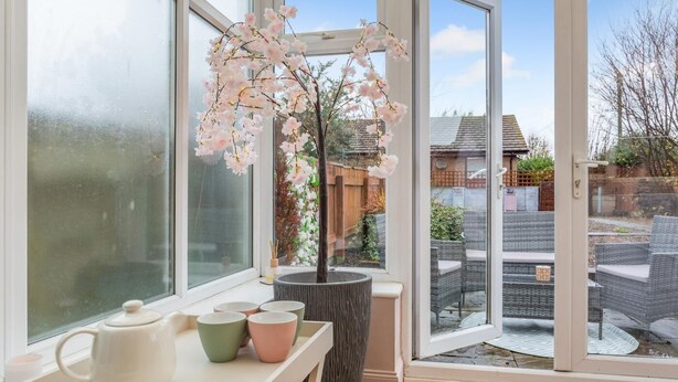 Een kamer met een groot raam, een tafel met kopjes en een potplant met roze bloemen.