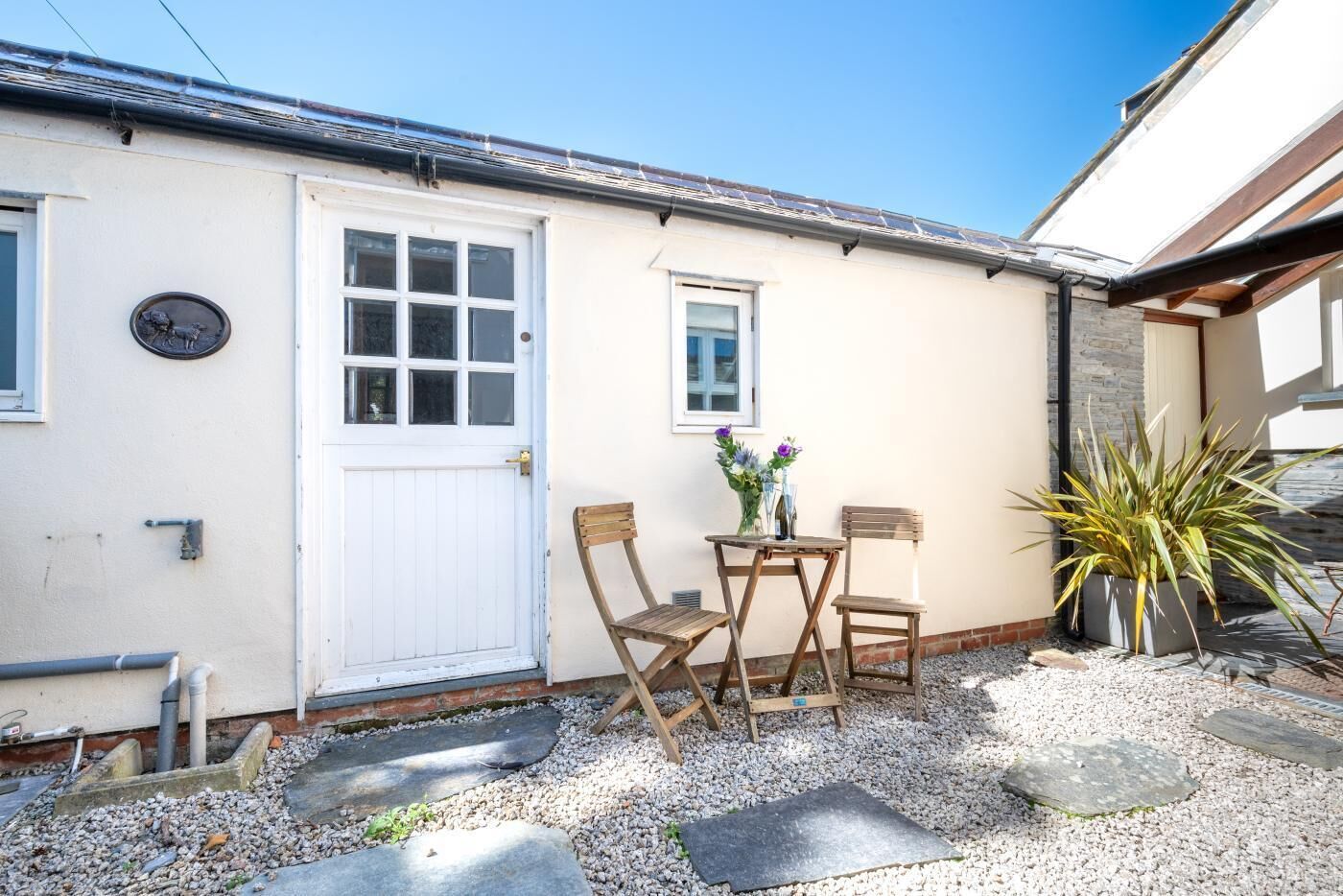 A house with a white door, a small window, and a patio with a table and chairs.