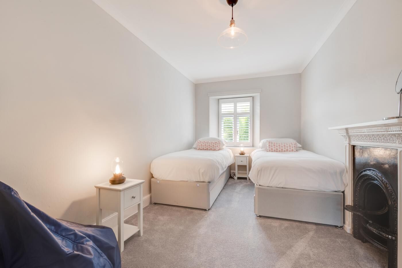 Ein Schlafzimmer mit zwei Betten, einem Nachttisch, einer Lampe, einem Fenster und einem Kamin.