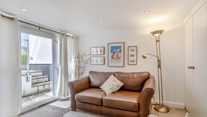 Een woonkamer met een bruine leren bank, een vloerlamp en ingelijste foto’s aan de muur.