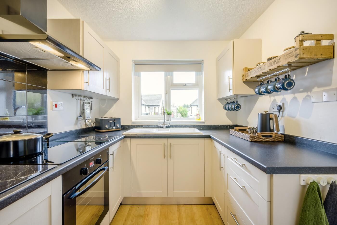 A compact kitchen with a window, a stove, a sink, and a countertop with various appliances.