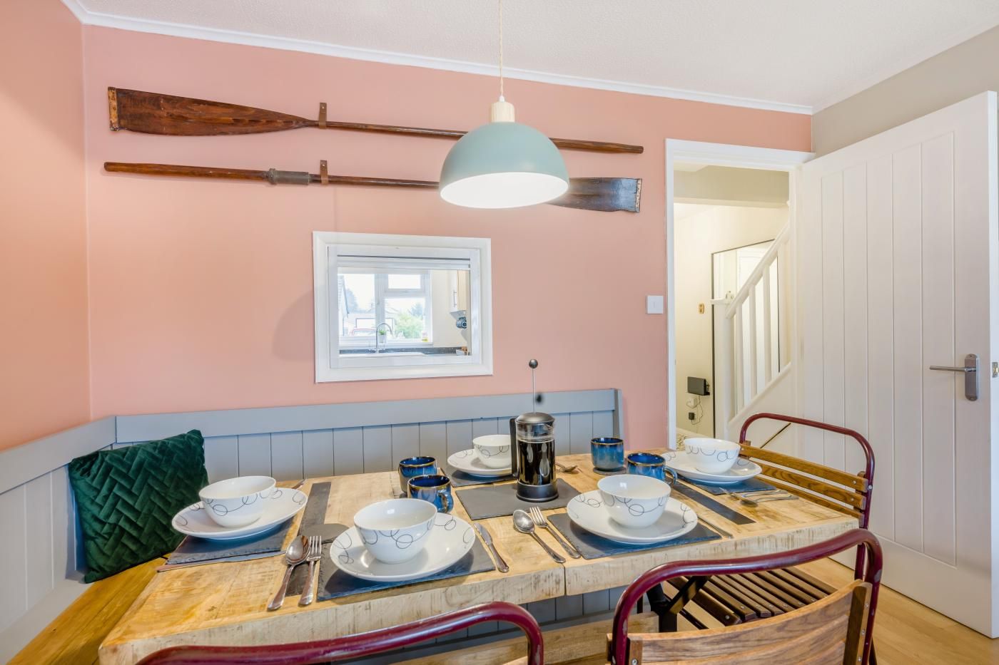 Un coin repas avec une table en bois dressée pour quatre personnes, un banc et un luminaire suspendu.