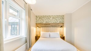 Een slaapkamer met een groot bed, twee nachtkastjes, een raam met gordijnen, een houten hoofdbord en behang met een bloemendesign.