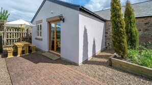A small, single-story building with a white exterior, a wooden door, and a small patio area with a table and benches. - 2 Bed in Milfield (oc-nb1982) (Milfield)