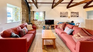 A living room with two red sofas, a wooden coffee table, a stone wall, a television, and artwork on the wall. - 2 Bed in Milfield (oc-nb1982) (Milfield)