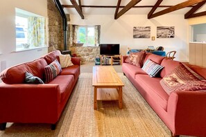 A living room with two red sofas, a wooden coffee table, a stone wall, a television, and artwork on the wall. - 2 Bed in Milfield (oc-nb1982) (Milfield)