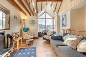 Ein gemütliches Wohnzimmer mit Holzbalken, einer Couch, einem Sessel und einem großen Fenster mit Blick.