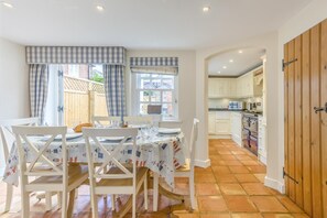 Un coin repas avec une table dressée pour quatre personnes, des chaises blanches et une fenêtre avec des rideaux.