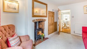 A cozy living room with a fireplace, a red sofa, and a hallway leading to another room. - 3 Bed in Southwold (oc-stan) (Southwold)