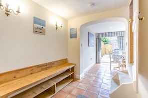 Ein Flur mit einer Bank, auf der 'Stannard Cottage Southwold' steht, einer Wandleuchte und einer Tür zu einem Patio.
