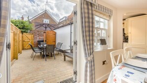 A patio with a table and chairs, a wooden fence, and a brick wall. - 3 Bed in Southwold (oc-stan) (Southwold)