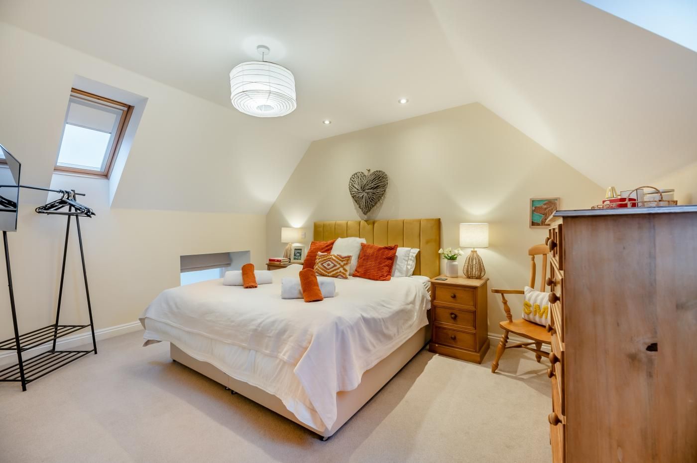 A bedroom with a large bed, a wooden dresser, a nightstand, and a ceiling light fixture.