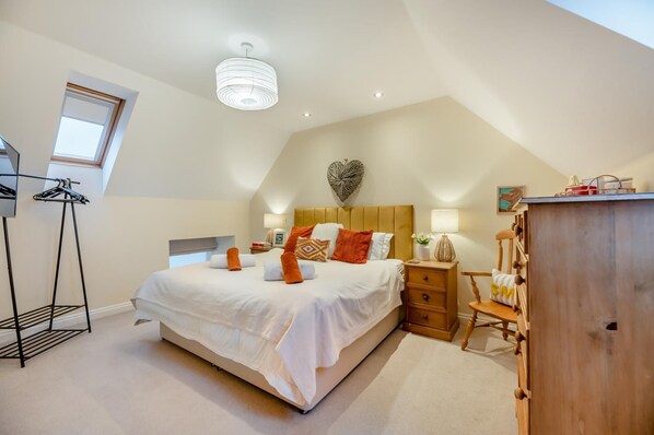 A bedroom with a large bed, a wooden dresser, a nightstand, and a ceiling light fixture.