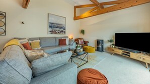 A modern living room with a sofa, a flat-screen TV, a wooden TV stand, a fireplace, and a ceiling with exposed beams.