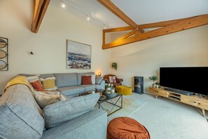 A modern living room with a sofa, a flat-screen TV, a wooden TV stand, a fireplace, and a ceiling with exposed beams.