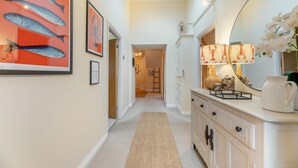 A hallway with a carpet, a mirror, framed artwork, and a lamp.