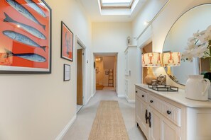 A hallway with a carpet, a mirror, framed artwork, and a lamp.